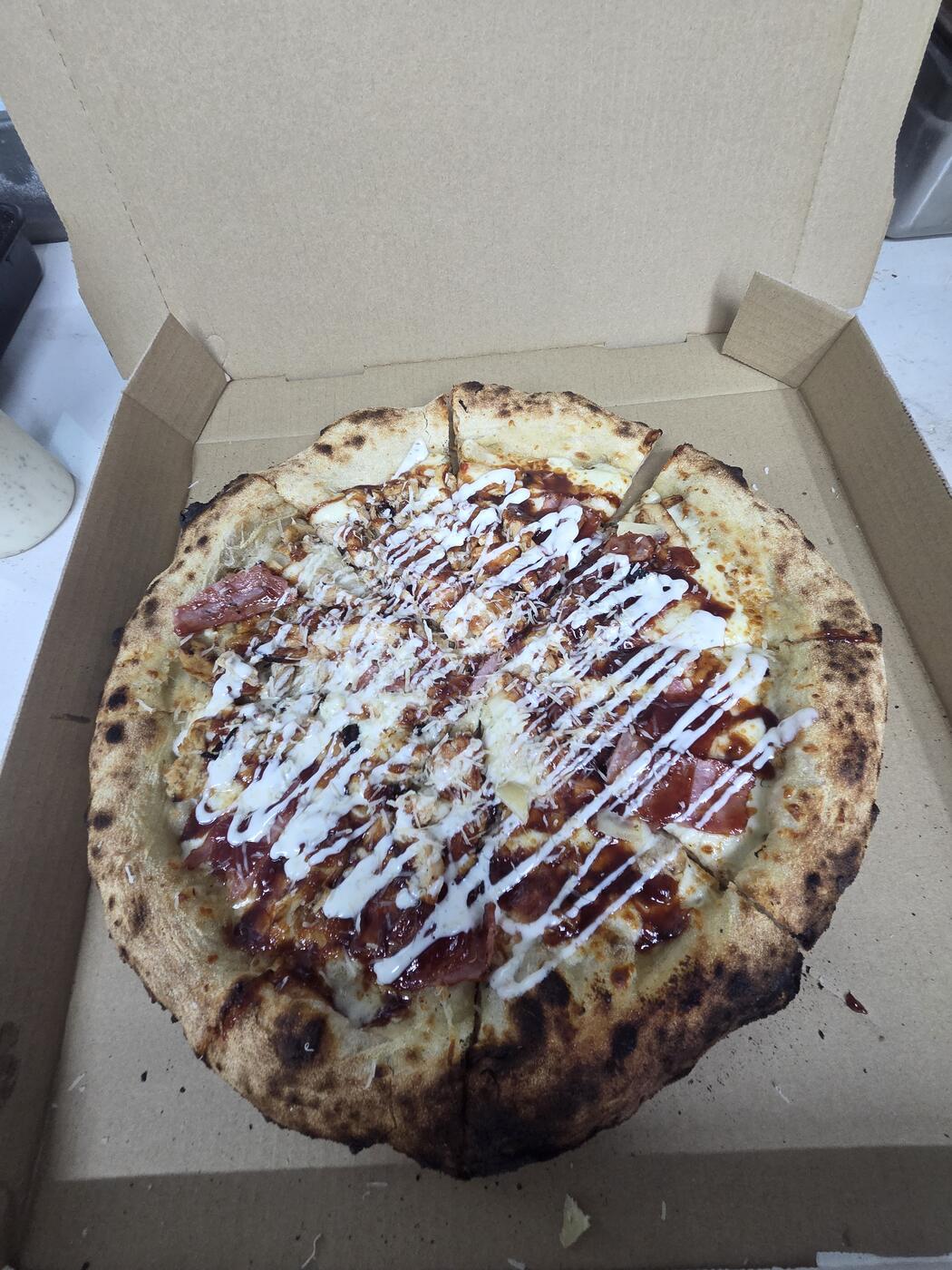 Pizza with chicken, ham, a red sauce, and a white drizzle